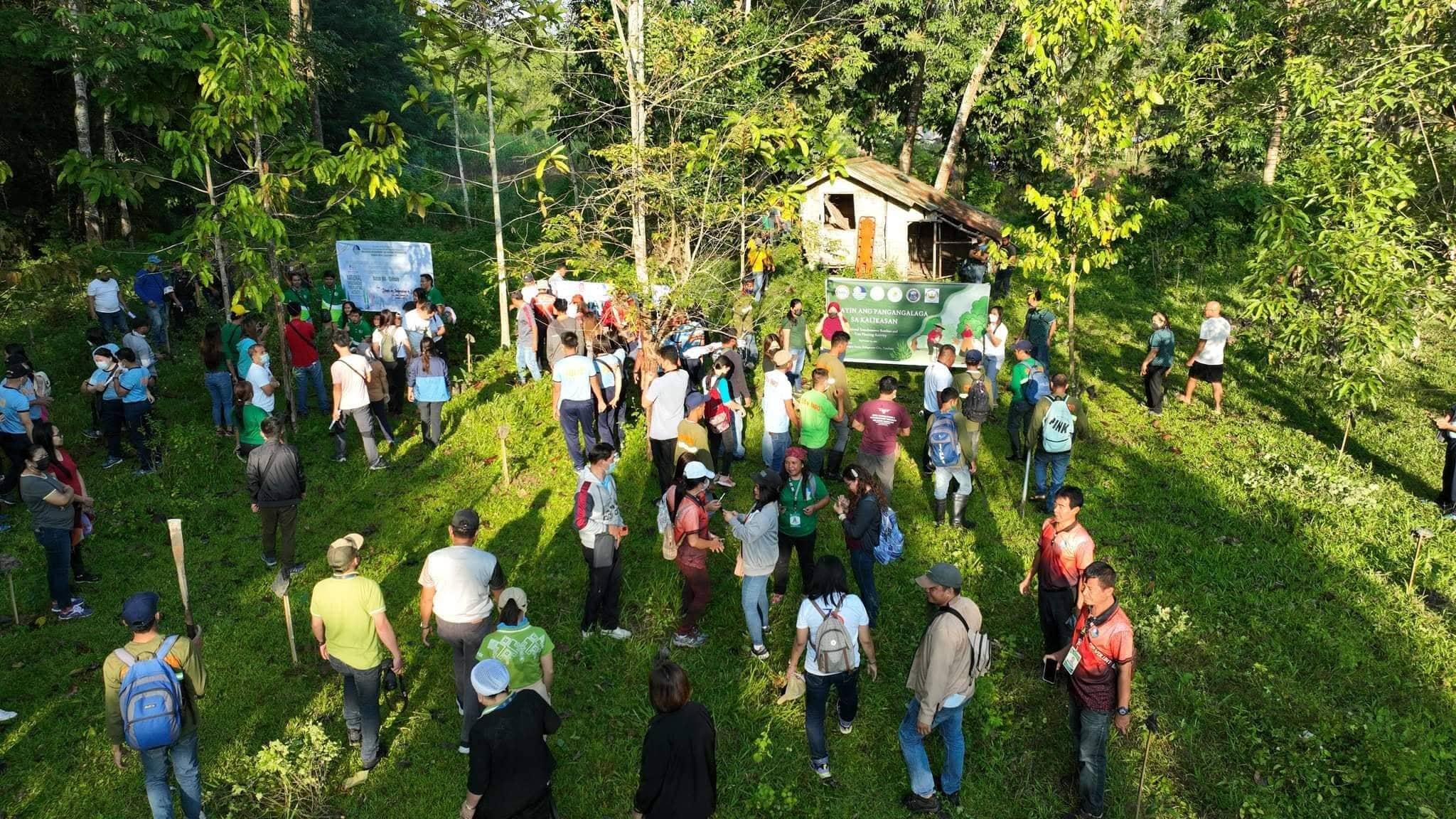 Aerial view of a large group assembled at a planting site, banners set up among the young trees